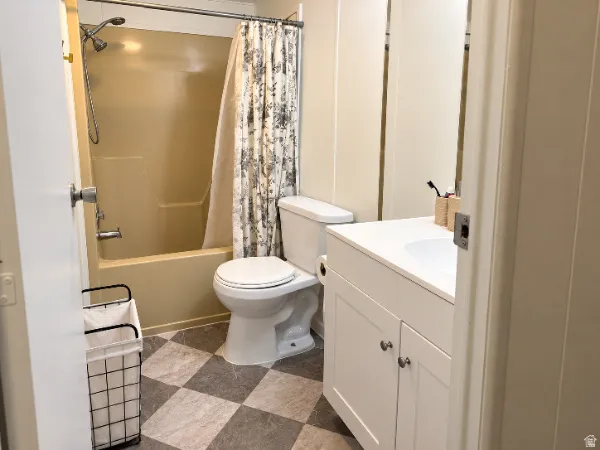 White vanity with integrated sink, checkerboard flooring, and a shower-over-tub combination