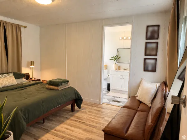 Wood-finish flooring, white panel walls, and an attached bathroom with a single vanity and wall-mounted light fixture