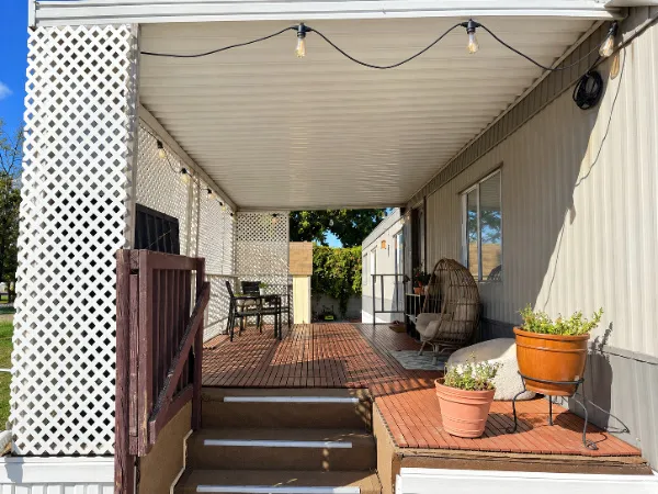 Covered porch with wood-finish decking, white lattice fencing, exterior lighting, and an additional porch entry