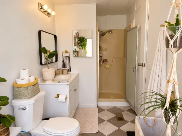White vanity with integrated sink, overhead vanity lighting, framed mirror, and a standing shower enclosure
