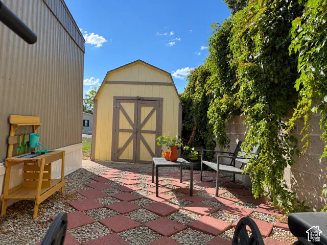 Detached storage shed with double doors, established climbing greenery on a perimeter wall, and a patterned paver and gravel patio area