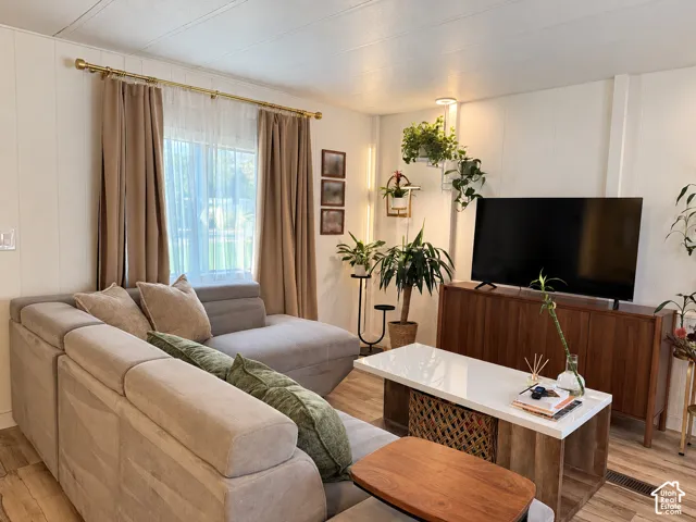 Recessed lighting illuminates wood-finish flooring and a window with a sheer curtain and solid drapes