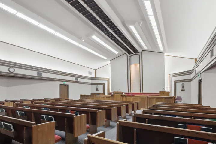 High ceilings with recessed linear lighting, wood-finish pews, and a raised platform with wood-finish pulpits