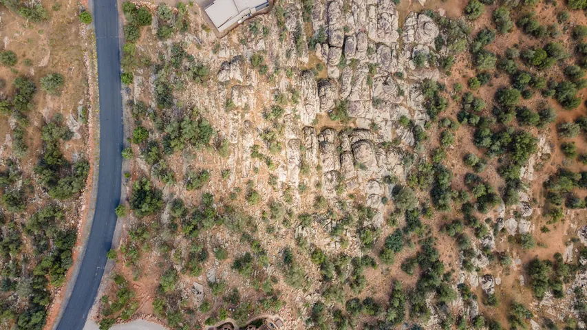 Winding paved road, natural rock formations, scattered natural vegetation, arid landscape
