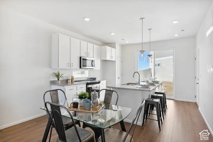 Kitchen featuring white cabinetry, stainless steel appliances, granite-style countertops, an island with seating, and wood-finish flooring