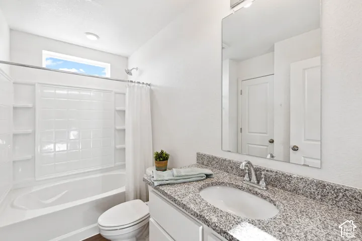 Bathtub with integrated shelving, chrome showerhead, rectangular window, vanity with granite countertop, and undermount sink