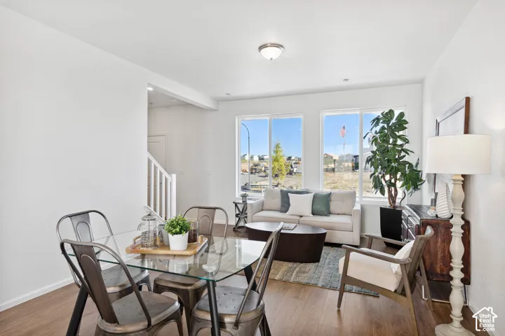 Open-concept living area with wood-finish flooring, white walls, and a glass-top dining table