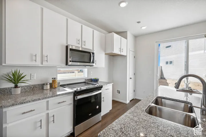 White cabinetry with brushed nickel hardware, stainless steel appliances, granite countertops, recessed lighting, and wood-finish flooring