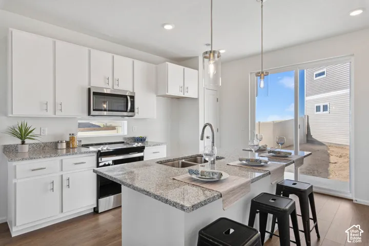 Kitchen featuring white cabinetry, stainless steel appliances, granite countertops, and wood-finish flooring
