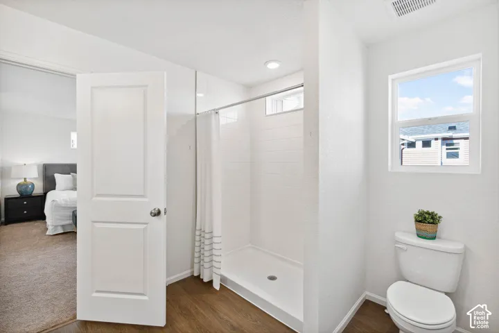 Shower with tiled surround, wood-finish flooring, and a window