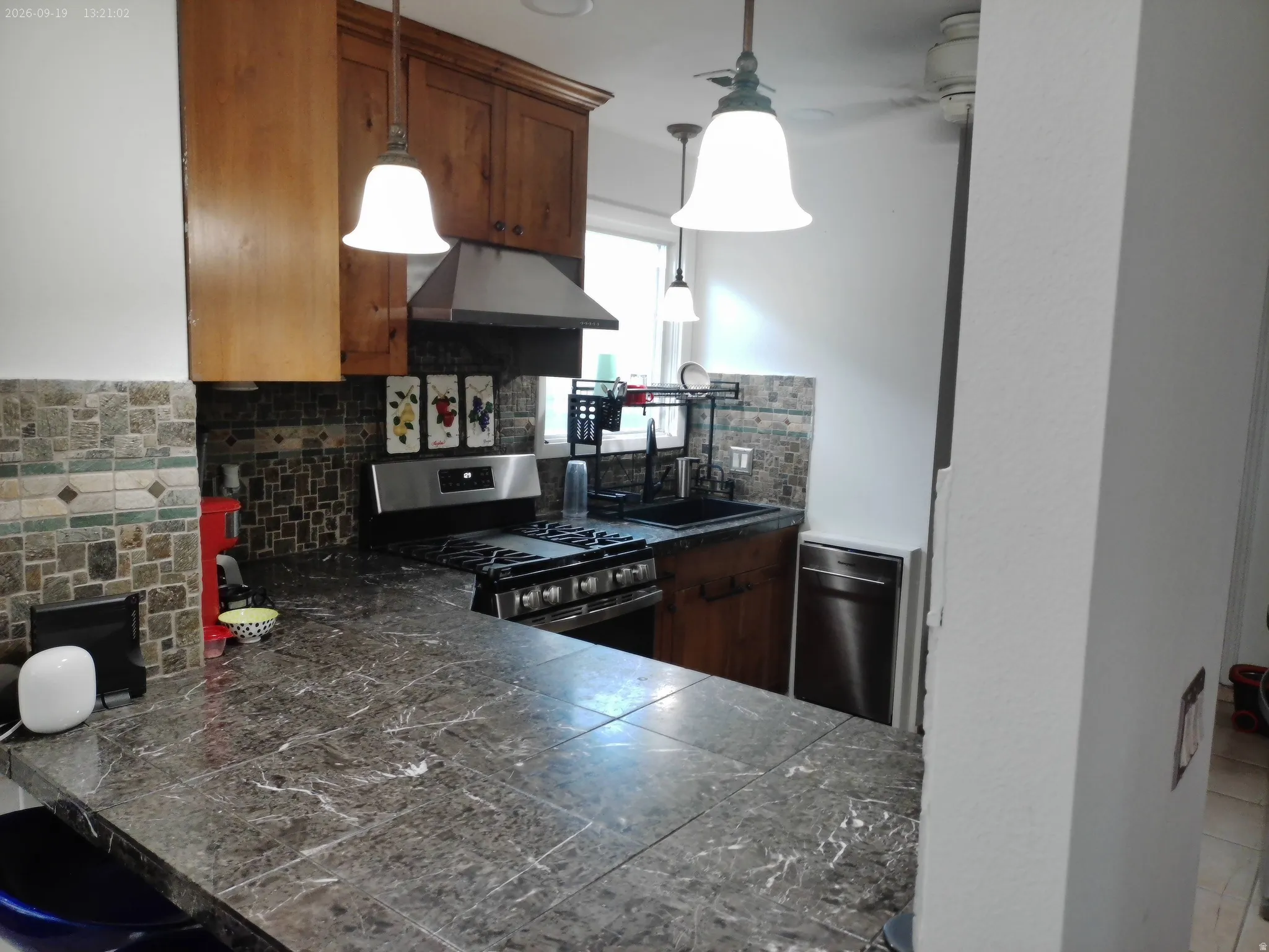 Kitchen featuring wood cabinetry, stainless steel appliances, mosaic tile backsplash, pendant lighting, and a tiled countertop