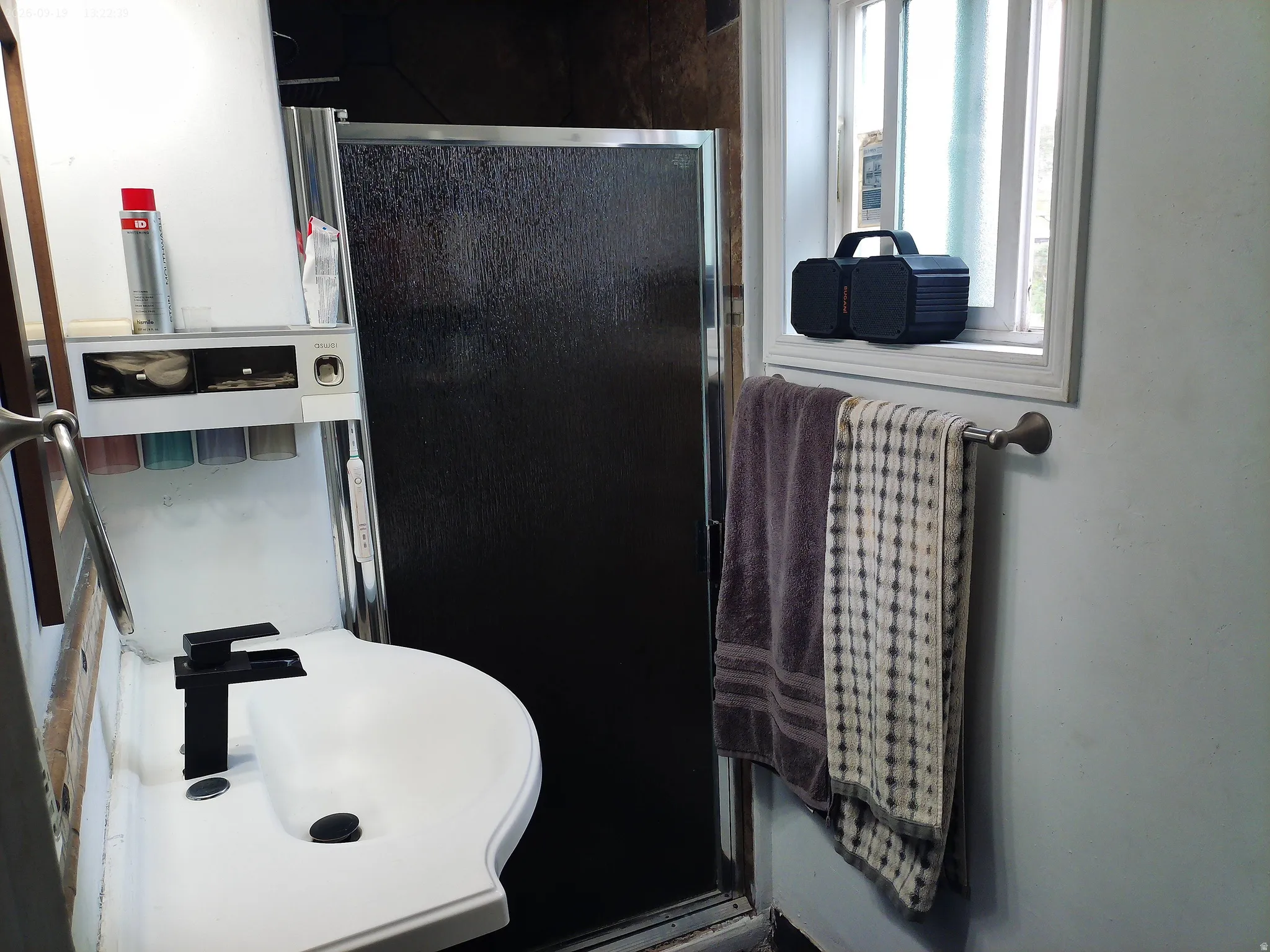 Compact bathroom featuring a shower enclosure, a single window, and a wall-mounted towel bar