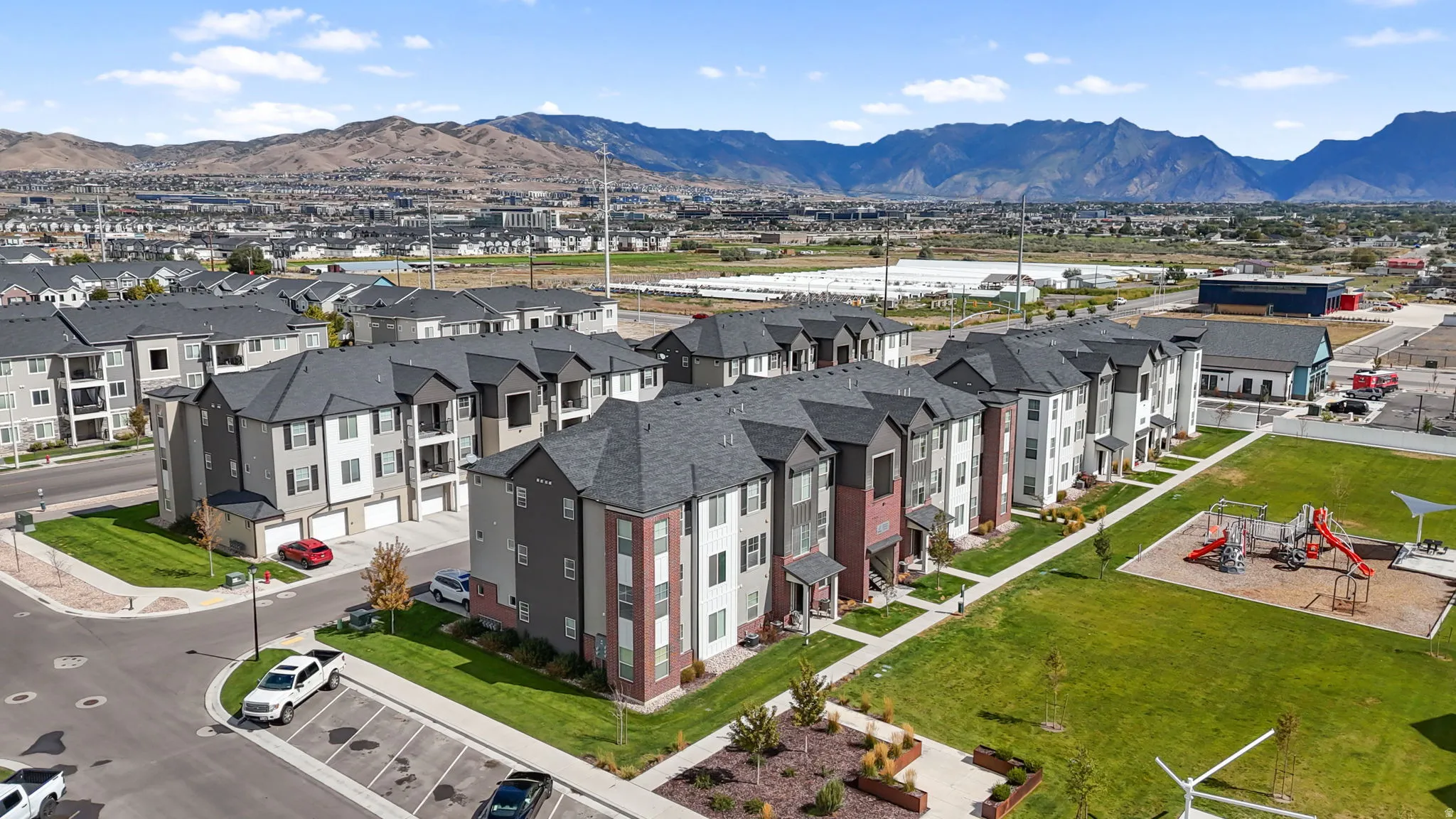Modern residential development with mountain backdrop, featuring multi-story buildings, dedicated parking, and manicured green spaces