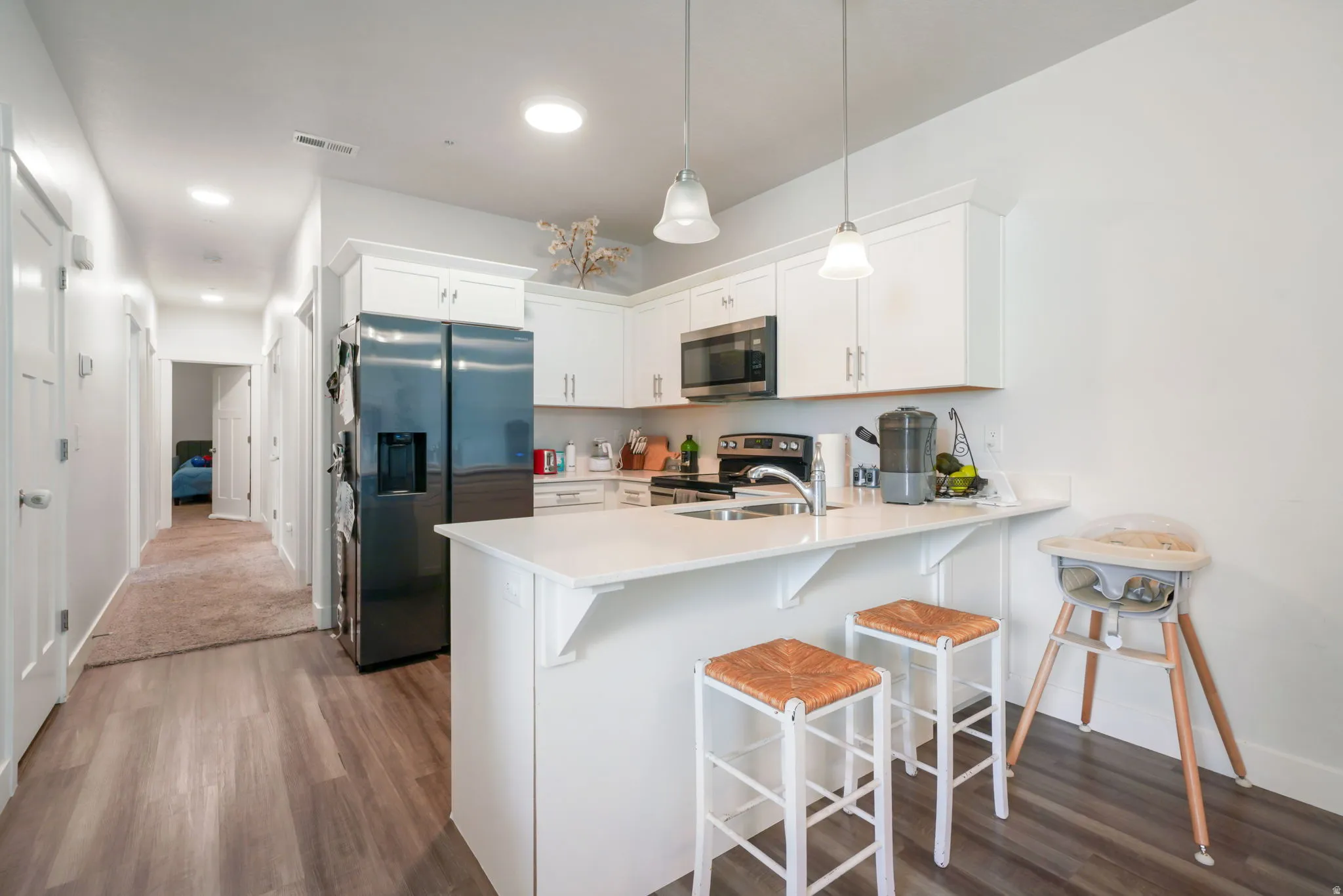 Kitchen featuring white cabinetry, stainless steel appliances, a white island with breakfast bar, pendant lighting, and wood-finish flooring