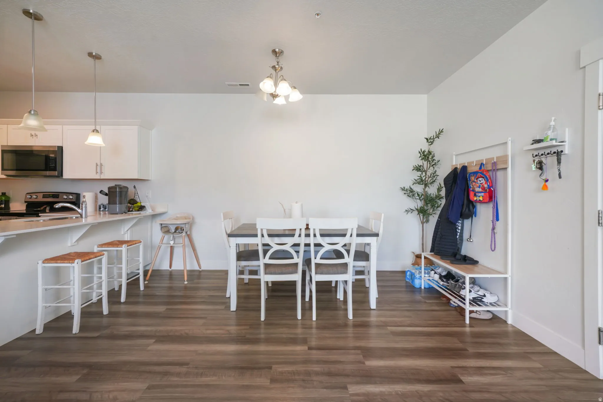 Open concept living area featuring wood-finish flooring, white cabinetry, a kitchen island with seating, pendant lighting, and a dining area