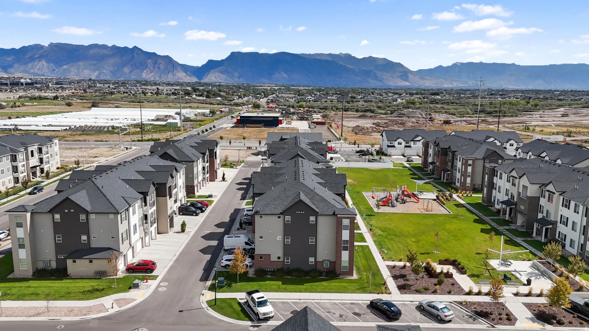 Community featuring multi-story residential buildings, an expansive central lawn, dedicated playground area, and paved roadways with structured parking