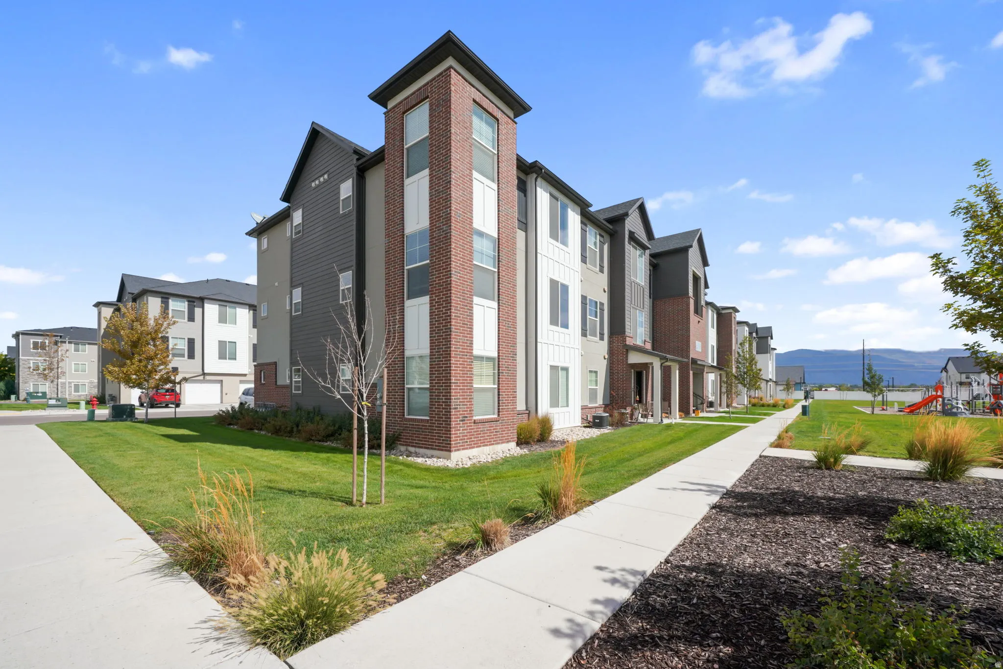 Multi-story building featuring brick and siding facade, multiple windows, covered entrances, and a manicured lawn with a concrete walkway