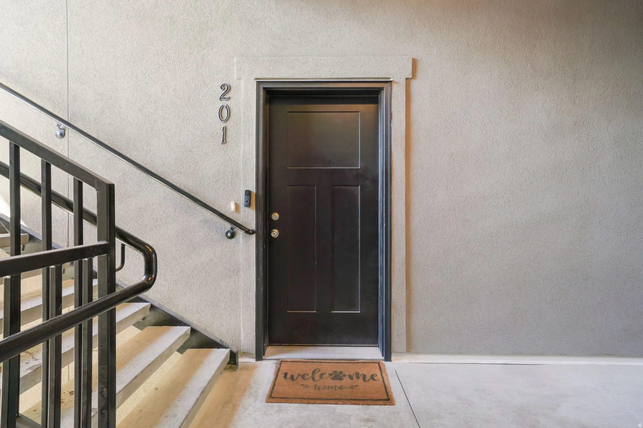 Dark-paneled entry door, modern black railing, concrete staircase, and textured wall finish