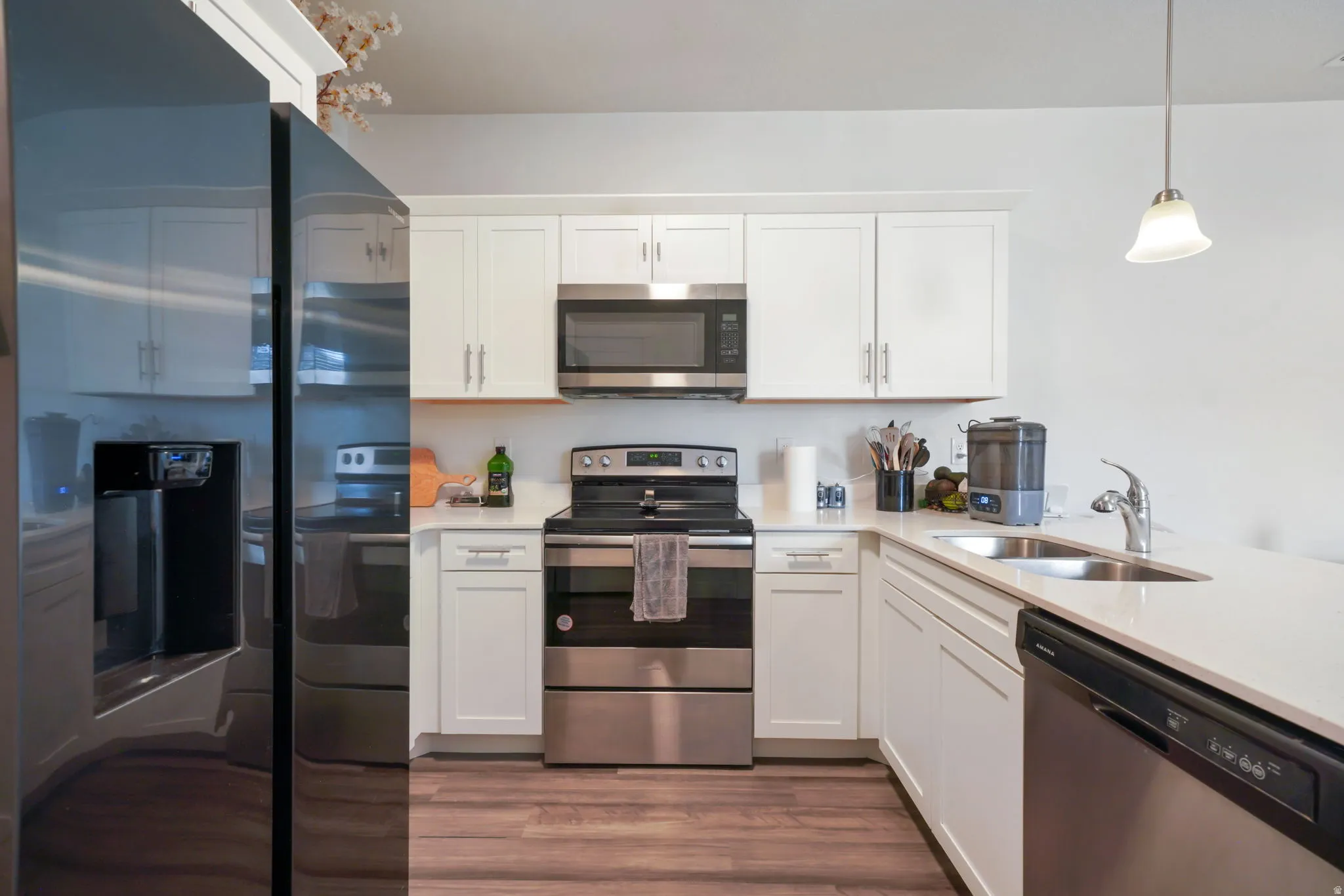 White shaker cabinetry with brushed nickel hardware, stainless steel appliances, quartz countertops, a double basin sink, and wood-finish flooring