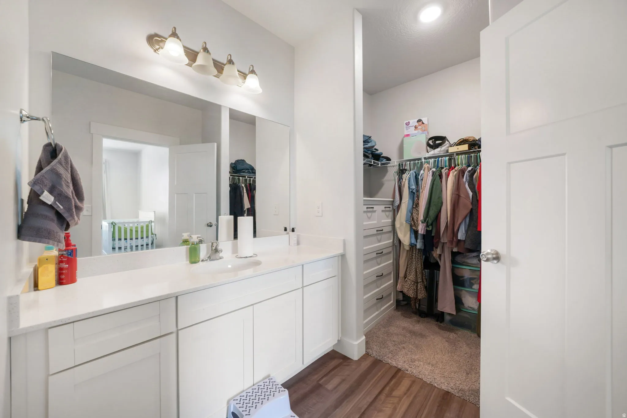 White cabinetry with a single undermount sink, a large vanity mirror, and a built-in closet with wire shelving