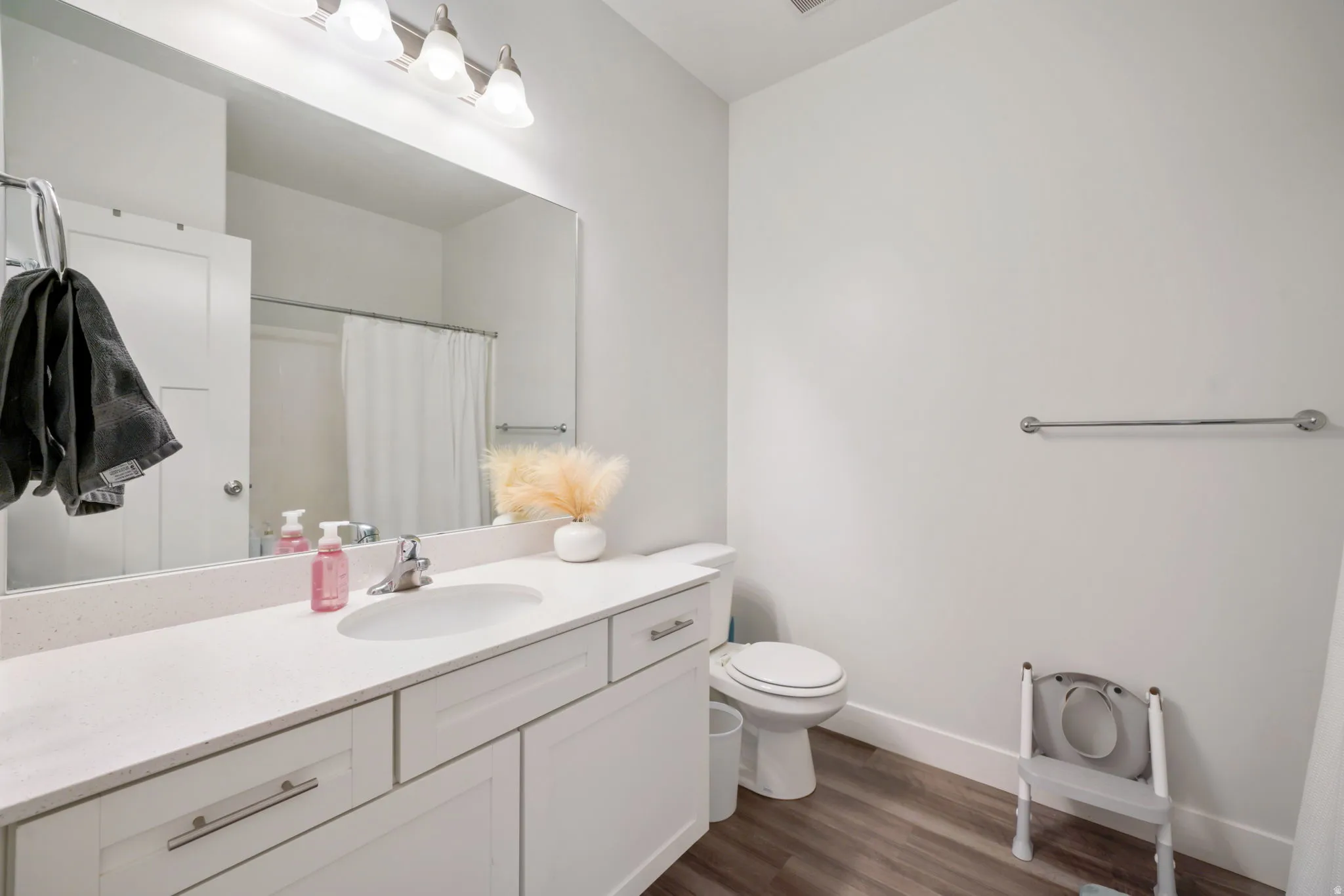 Spacious bathroom featuring a white vanity with an integrated sink, a large wall-mounted mirror, and wood-finish flooring