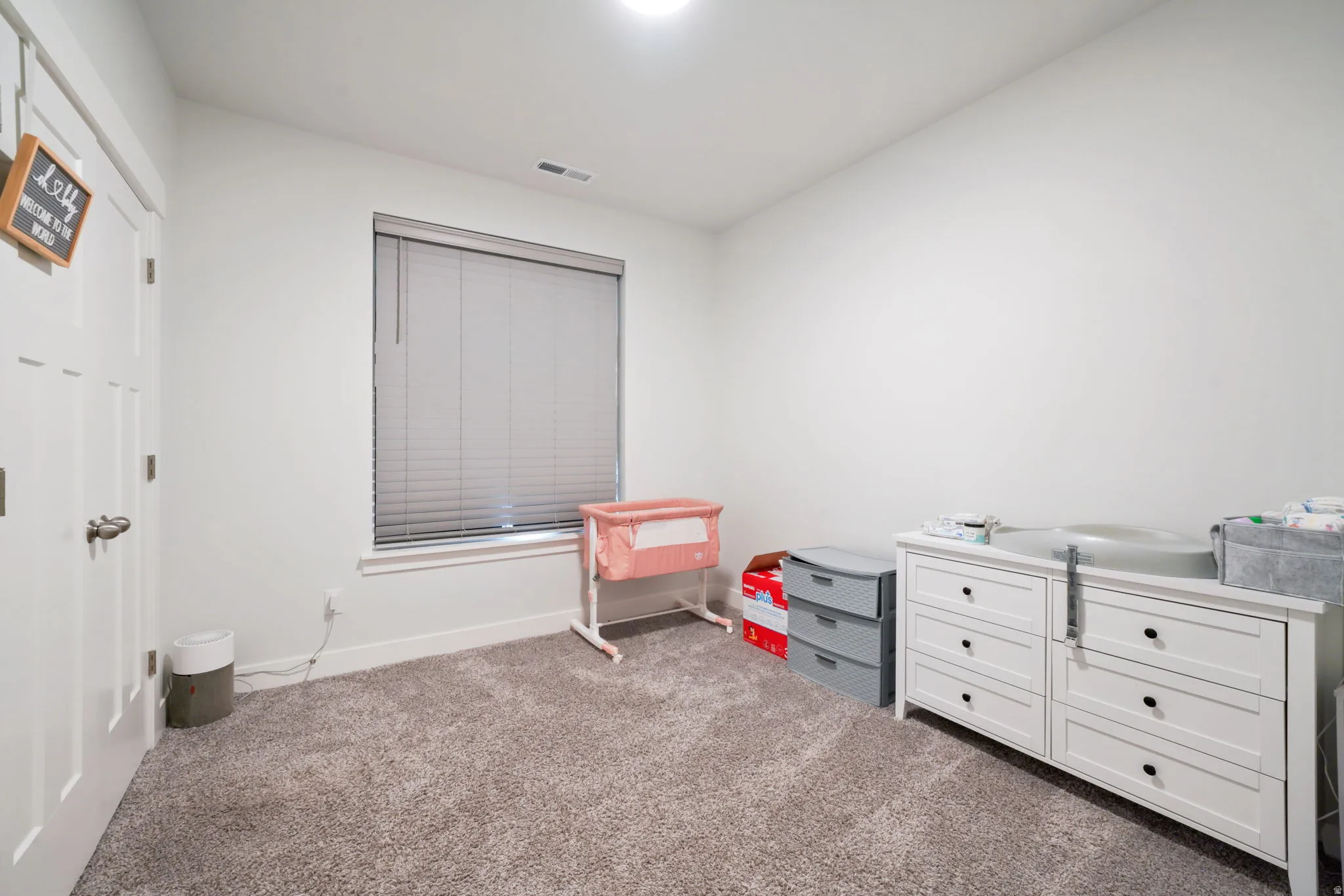 White painted walls, gray carpet flooring, and a single window with blinds
