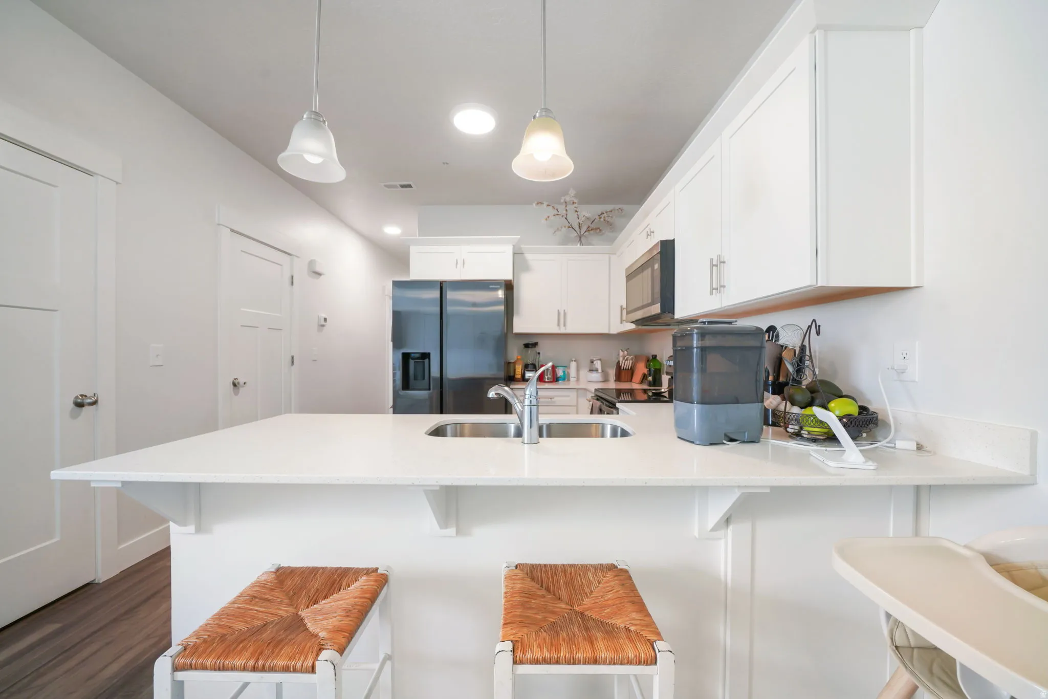 Kitchen featuring a peninsula with integrated sink, white cabinetry, stainless steel appliances, and ceiling-mounted pendant lighting