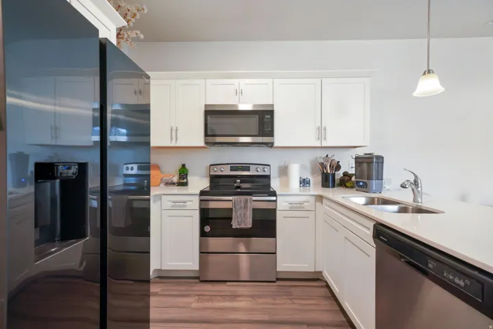 White shaker cabinetry with brushed nickel hardware, stainless steel appliances, quartz countertops, a double basin sink, and wood-finish flooring