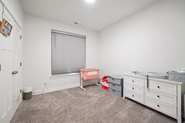 White painted walls, gray carpet flooring, and a single window with blinds