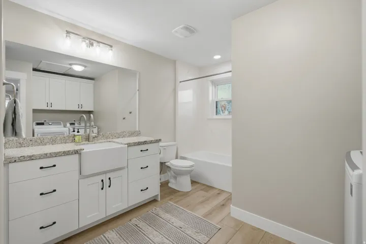 White shaker-style cabinetry with matte black hardware, granite-style countertop, farmhouse-style sink, and wood-finish flooring