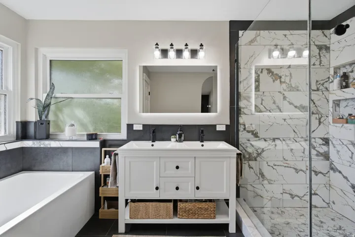 White double vanity with integrated sinks, backlit mirror, and modern lighting fixture