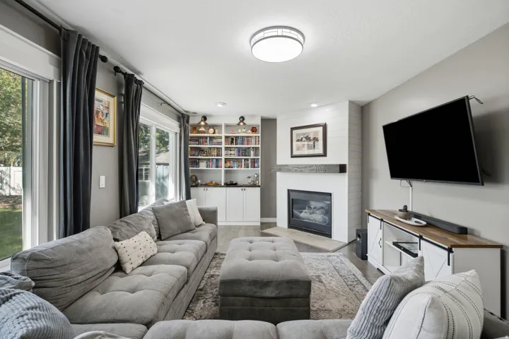 Built-in shelving with integrated lighting, shiplap fireplace surround, natural wood mantel, and sliding glass doors