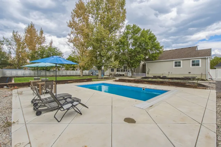 In-ground swimming pool with a concrete patio surround, bordered by a raised garden bed