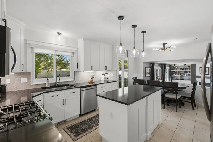 White cabinetry with matte black hardware, dark countertops, a tile backsplash, and stainless steel appliances