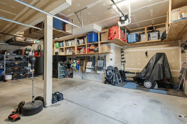 Spacious garage featuring concrete flooring, built-in overhead storage shelves, built-in wall shelving, and an automatic garage door opener