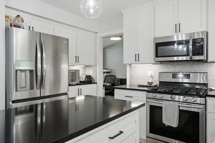 White shaker-style cabinetry, dark countertops, stainless steel appliances, honeycomb tile backsplash, and under-cabinet lighting