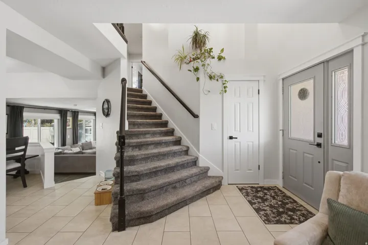 Tiled entryway flooring with a carpeted staircase and dark wood banister