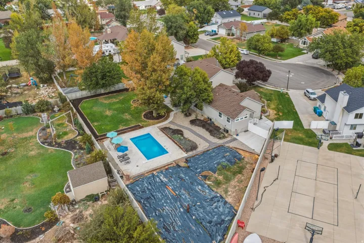 Expansive property featuring a rectangular swimming pool with surrounding concrete patio, a dedicated paved court area, a manicured lawn, and mature trees