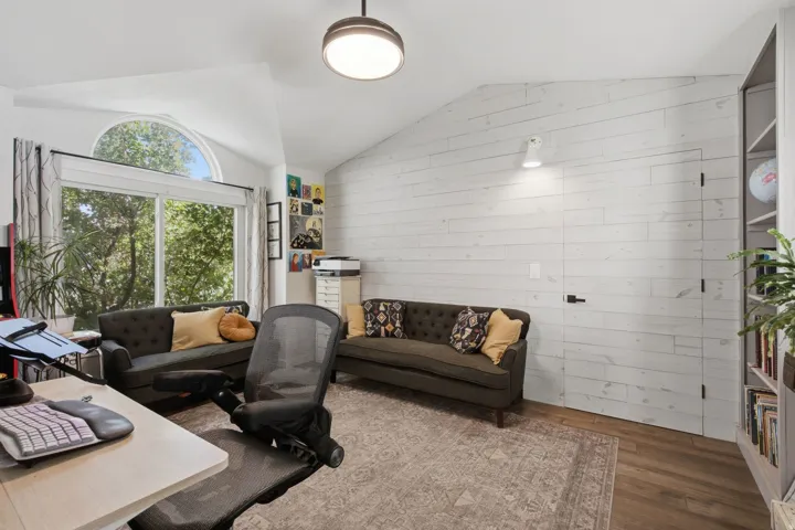Vaulted ceiling, wood-finish flooring, full-light glass doors with an arched transom, paneled accent wall, and built-in shelving