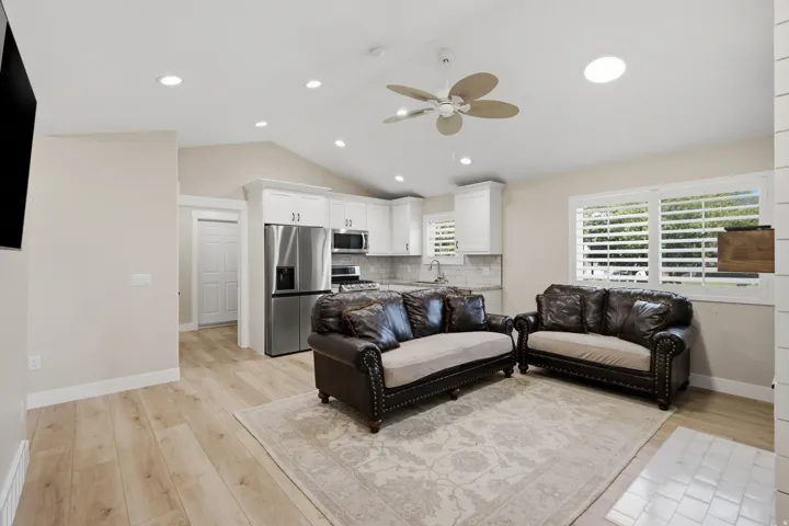 Vaulted ceiling with recessed lighting and ceiling fan, wood-finish flooring, white kitchen cabinetry, stainless steel appliances, and plantation shutters