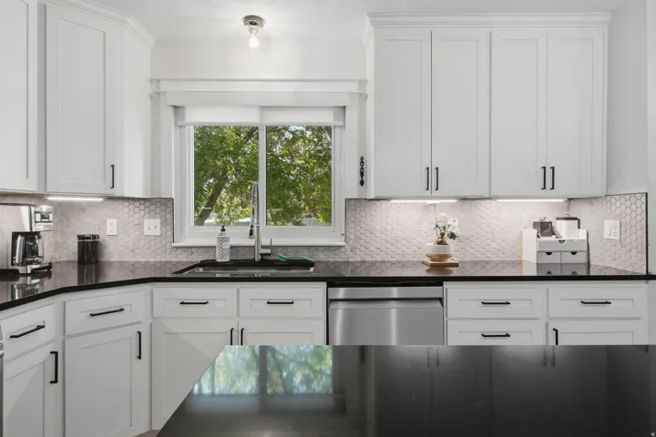 White shaker-style cabinetry, dark countertops, honeycomb tile backsplash, stainless steel dishwasher, and under-cabinet lighting