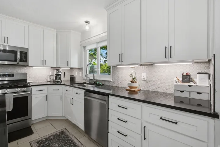 White shaker cabinetry, dark countertops, hexagonal tile backsplash, stainless steel appliances, and tile flooring