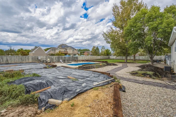 Outdoor swimming pool, gravel pathways, mature trees, white privacy fencing, and exterior wall siding