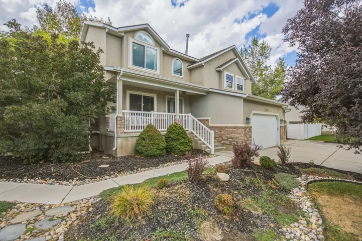 Stucco exterior with stone accent, arched windows, covered front porch, attached garage, and a concrete driveway