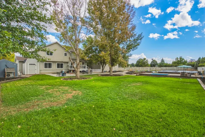 Expansive lawn area with mature trees, a dedicated patio space, and two detached storage sheds