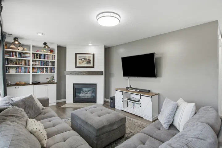 Built-in shelving with lower cabinetry, corner fireplace with wood mantle, plank wall accent, and wood-finish flooring
