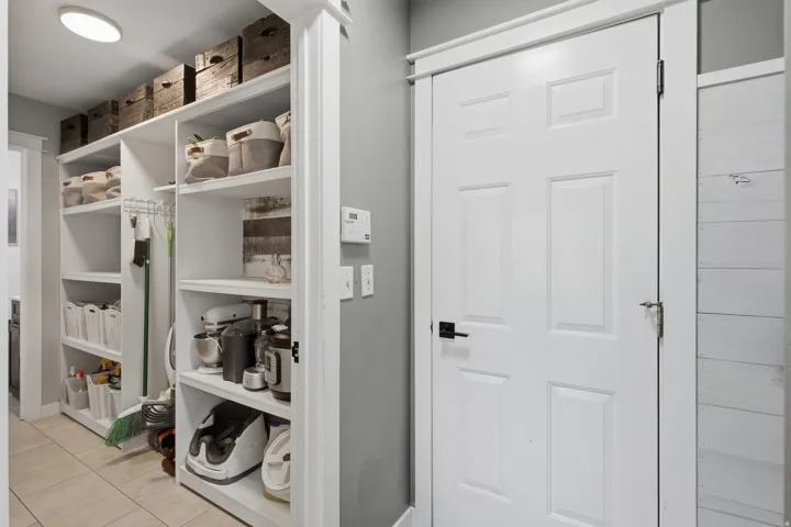 Floor-to-ceiling custom shelving, recessed ceiling light, paneled interior door, matte black door hardware, and light-toned floor tile