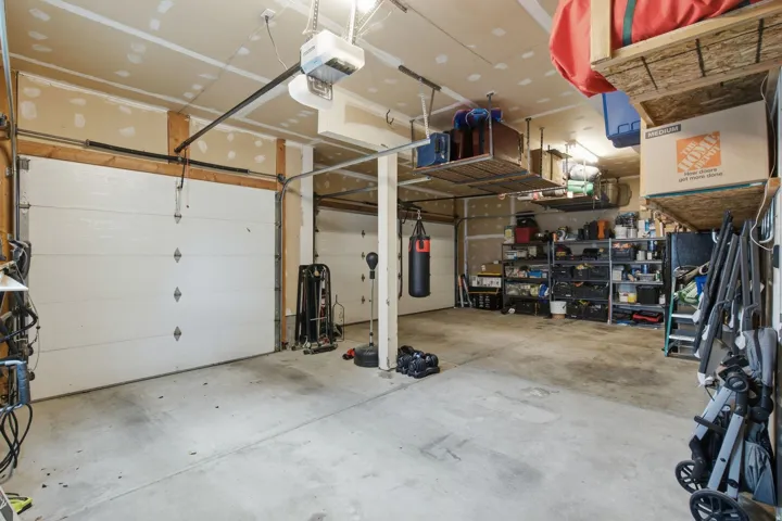 Two garage doors with automatic openers, overhead storage racks, and concrete flooring