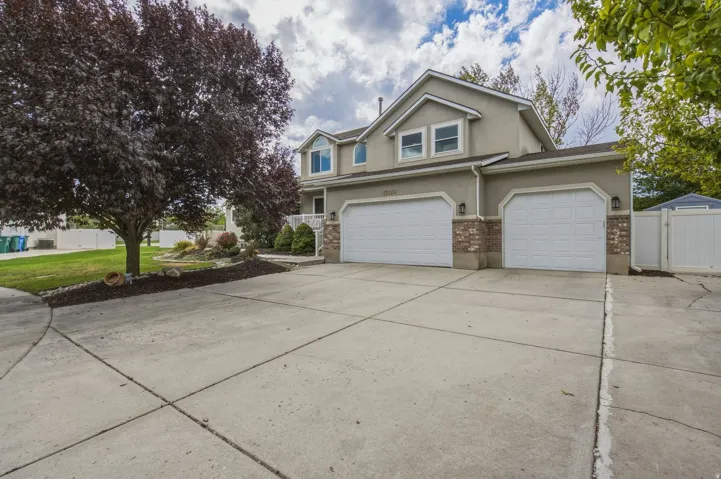 Stucco exterior with brick accents, two-car garage, concrete driveway, and mature landscaping