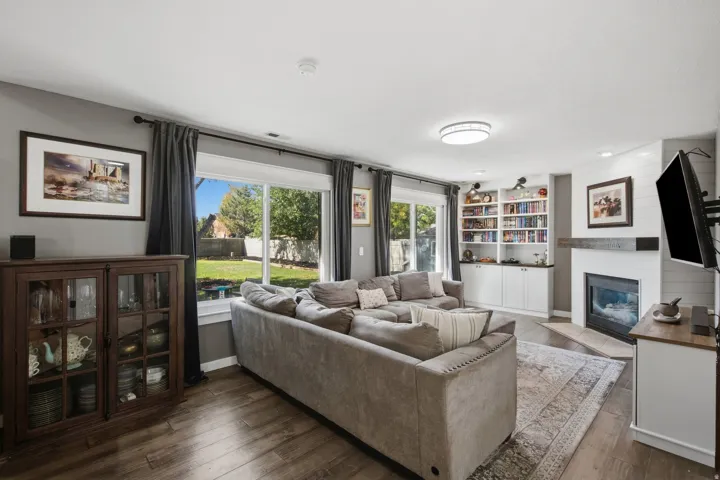 Wood-finish flooring throughout, built-in shelving, fireplace with a wood mantle, and a large window providing ample natural light